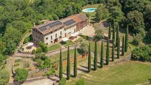 An aerial view of a large estate with a main building, a swimming pool, and a well-maintained garden with tall trees.