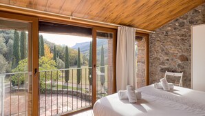 A bedroom with a large bed, a view of a garden, and a stone wall.