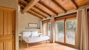 A bedroom with a wooden ceiling, a bed with white linens, a small bedside table, and a window with curtains.
