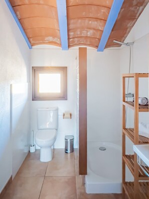 Bathroom features a toilet, shower with glass door, and a wooden shelf.