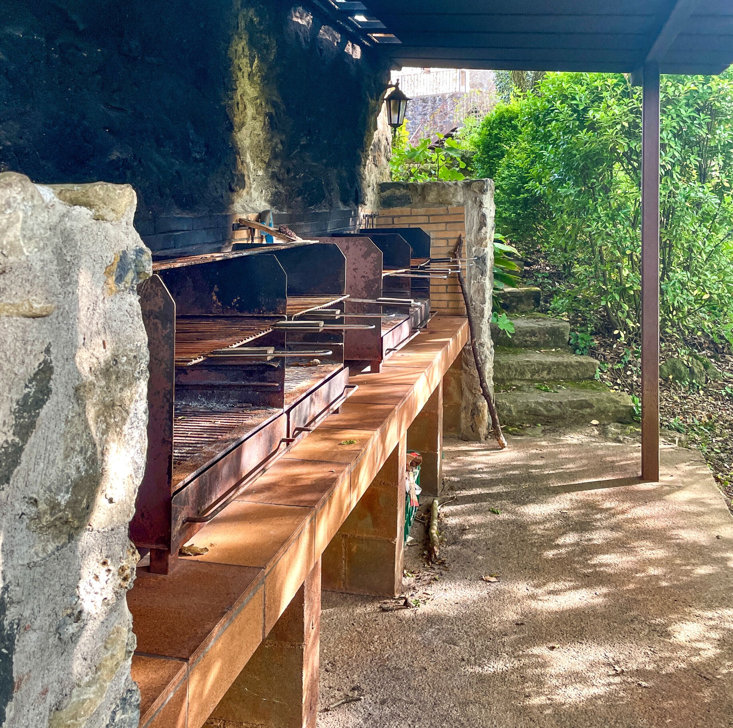 Un espace barbecue extérieur doté de plusieurs grils, d’un mur en pierre et d’un banc en bois.