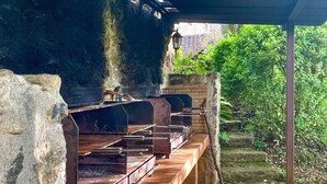 An outdoor barbecue area with multiple grills, a stone wall, and a wooden bench.
