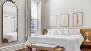 Un dormitorio con una cama grande, un banco al pie de la cama, un espejo y tres cuadros en la pared.