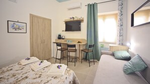 Une chambre à coucher avec un lit, un bureau, deux chaises, une télévision et une fenêtre avec des rideaux.