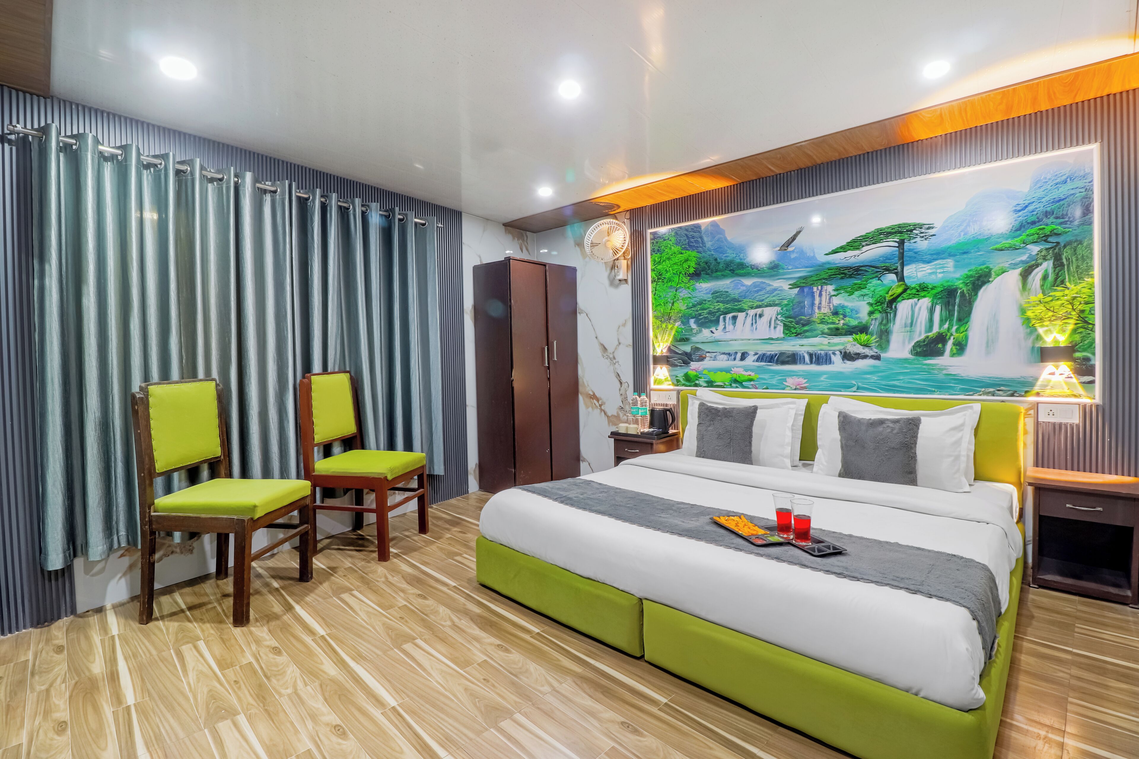 A hotel room with a bed, two chairs, a wardrobe, a nightstand, and a wall mural.