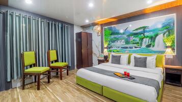 Quarto de hotel com uma cama, duas cadeiras, um guarda-roupa, uma mesinha de cabeceira e um mural na parede.