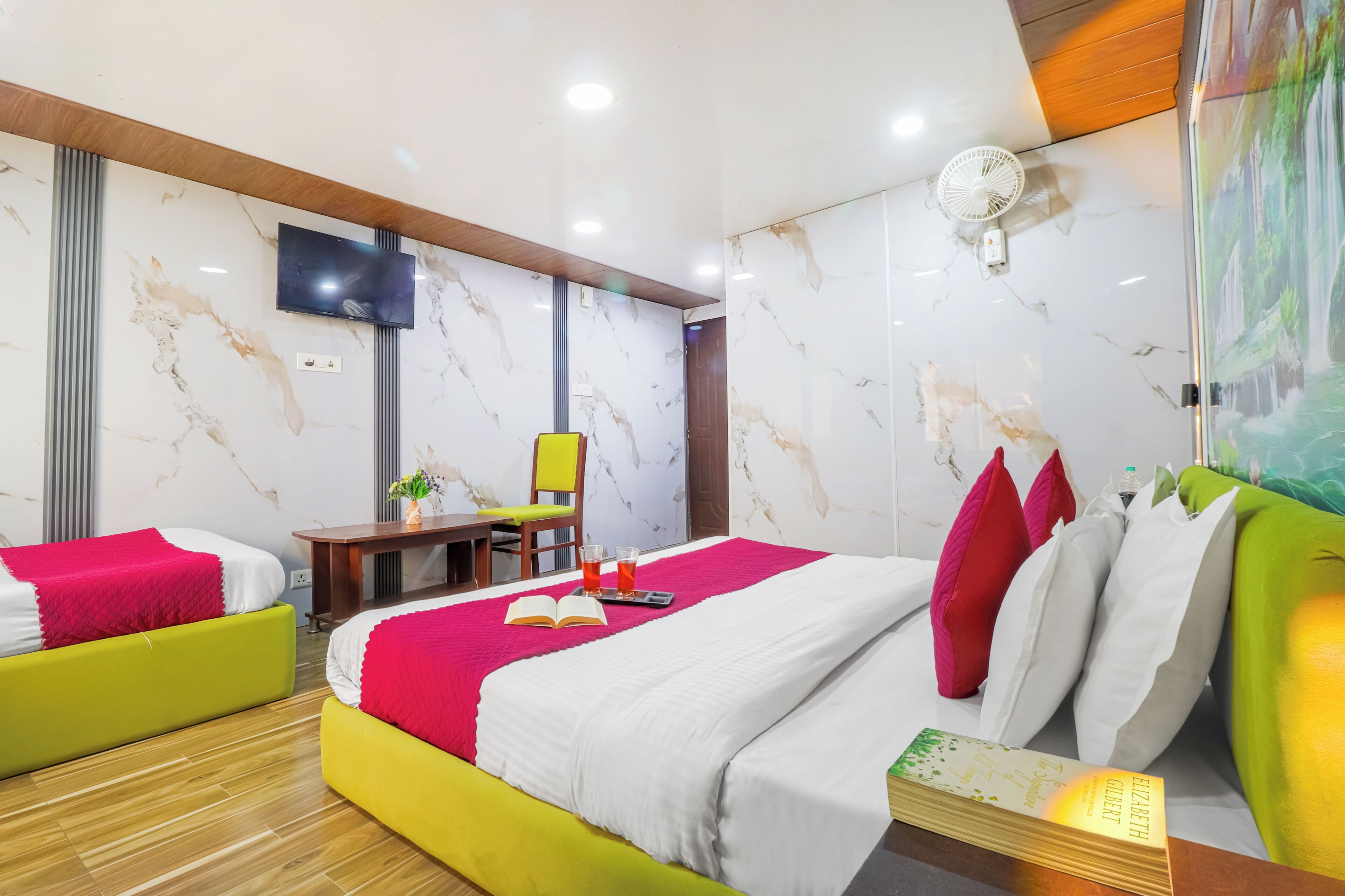 A hotel room with a bed, two sofas, a desk, a TV, and a fan.