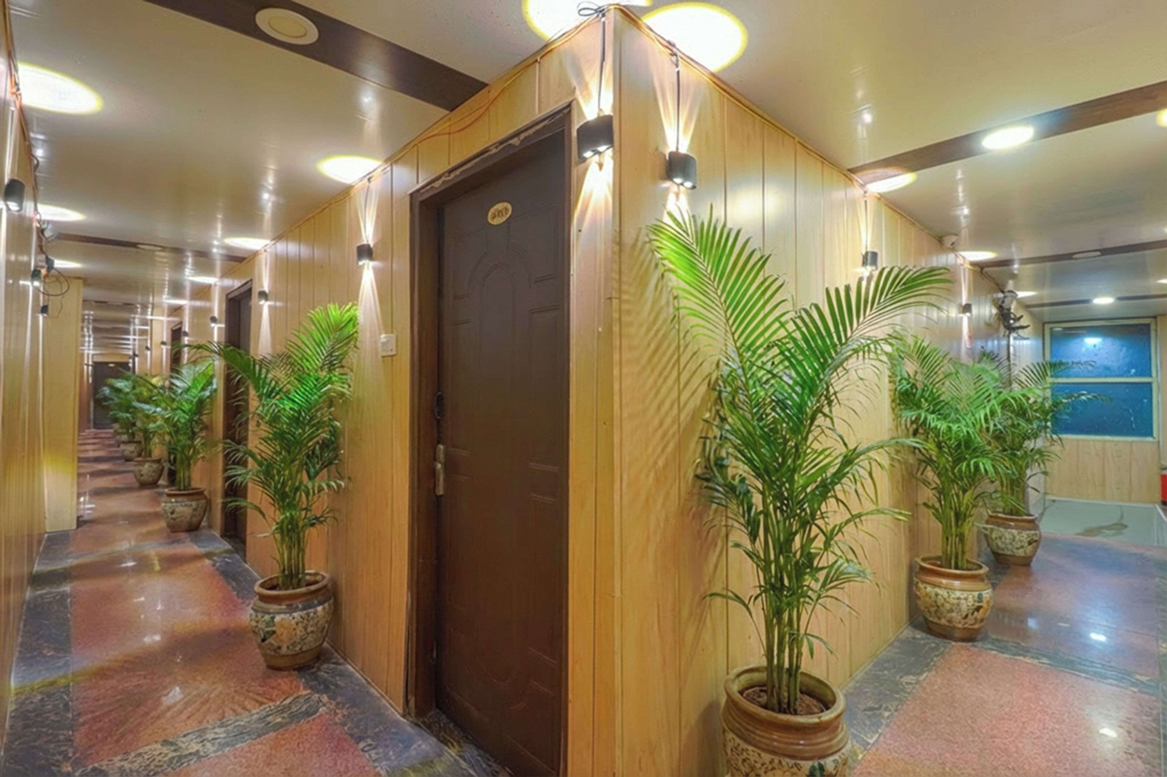 Un couloir aux murs recouverts de lambris en bois, agrémenté de plantes en pot et doté d’une porte sur laquelle est apposée une pancarte.