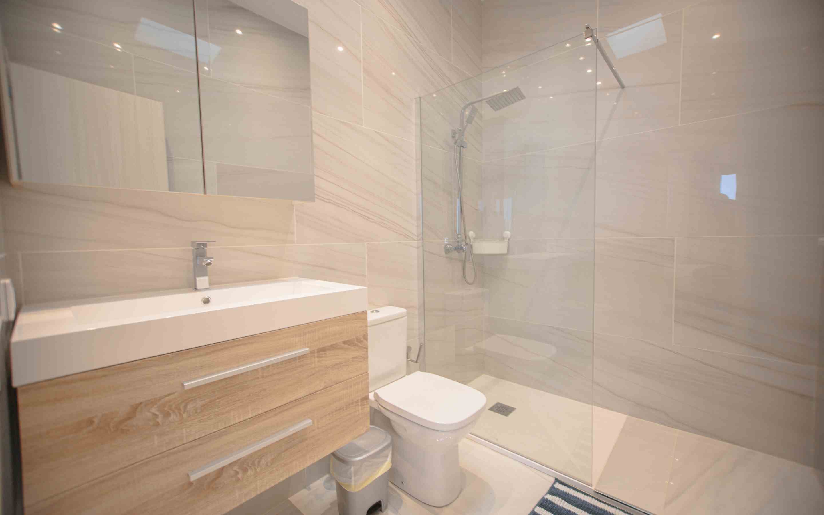 A modern bathroom with a glass-enclosed shower, a white sink, and a wooden vanity.