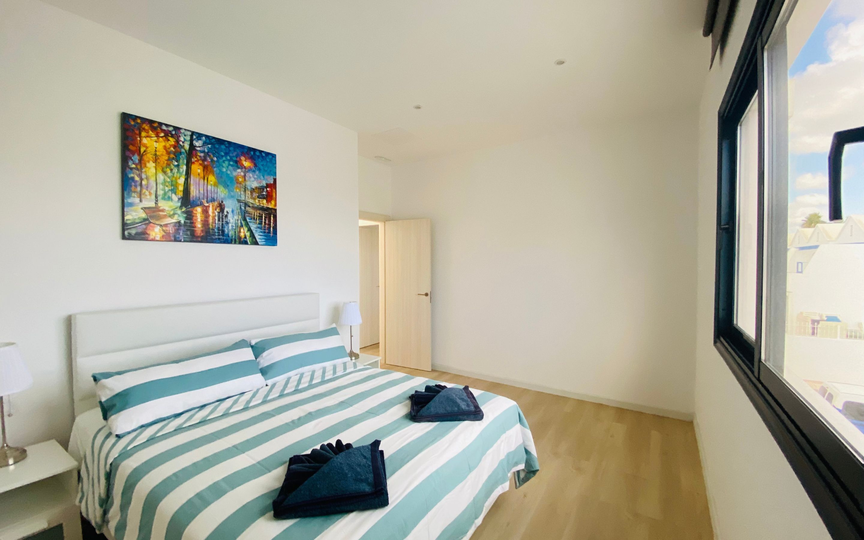 Habitación de hotel con cama, un cuadro en la pared y ventana con vistas a edificios.