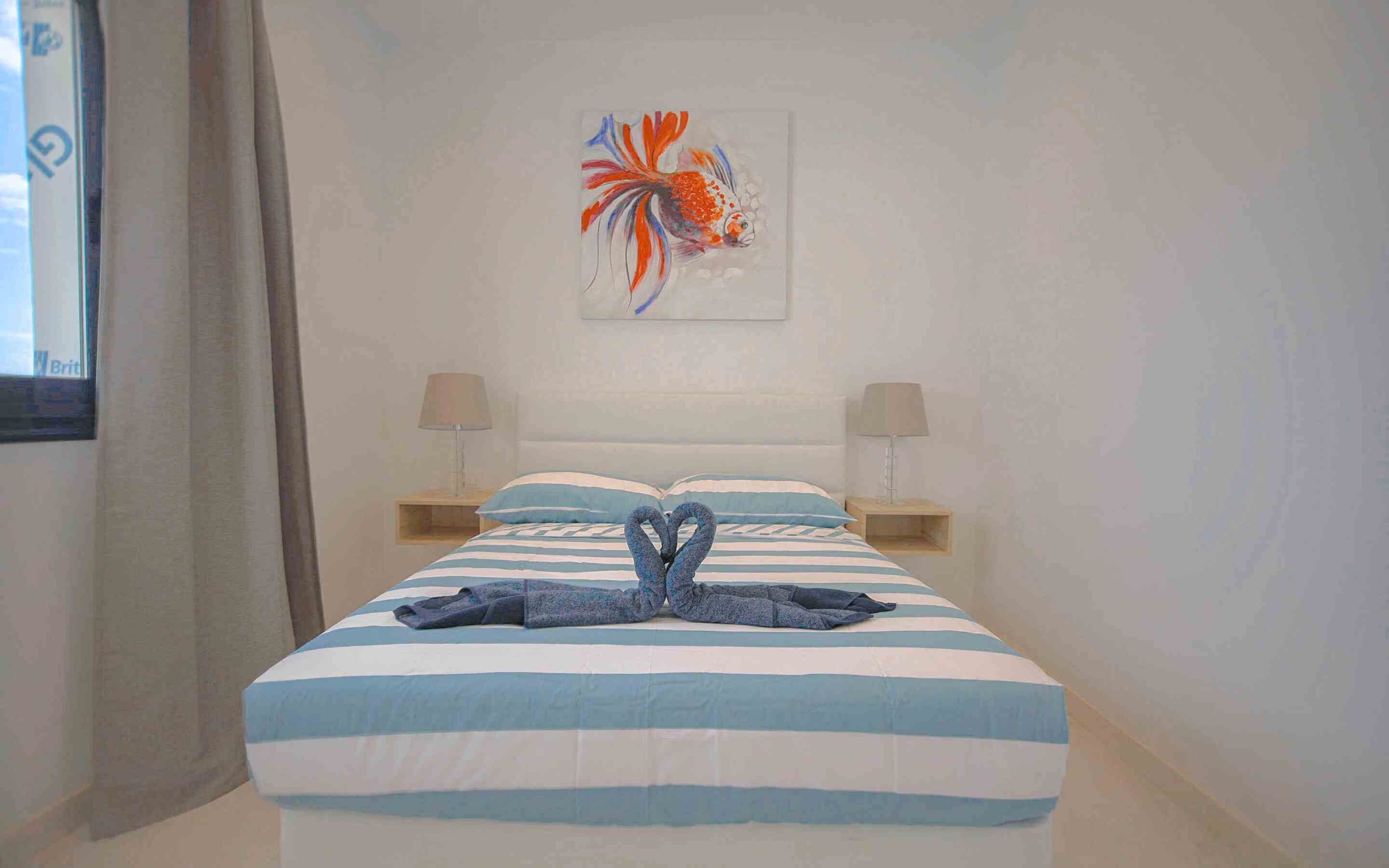 A hotel room with a bed, two bedside lamps, a painting, and a towel art on the bed.