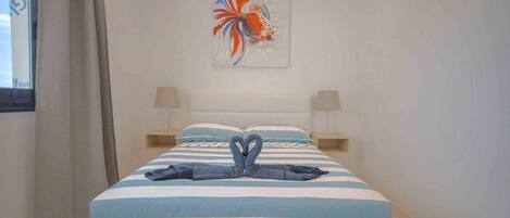 A hotel room with a bed, two bedside lamps, a painting, and a towel art on the bed.