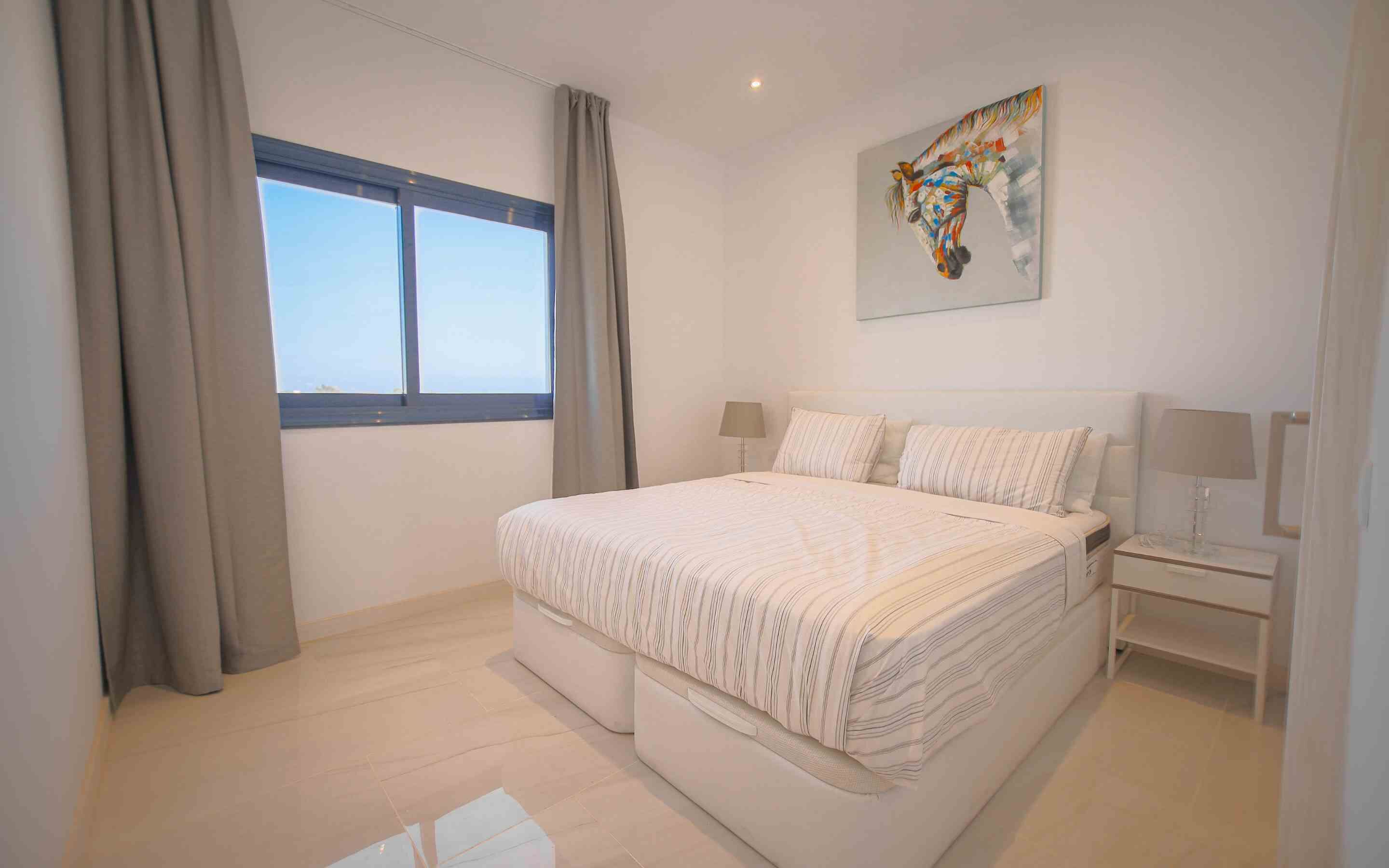 Une chambre à coucher avec un grand lit, deux tables de chevet, une fenêtre et un tableau au mur.