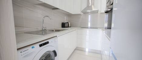 Een moderne keuken met witte kasten, een ingebouwde wasmachine en roestvrijstalen apparatuur.