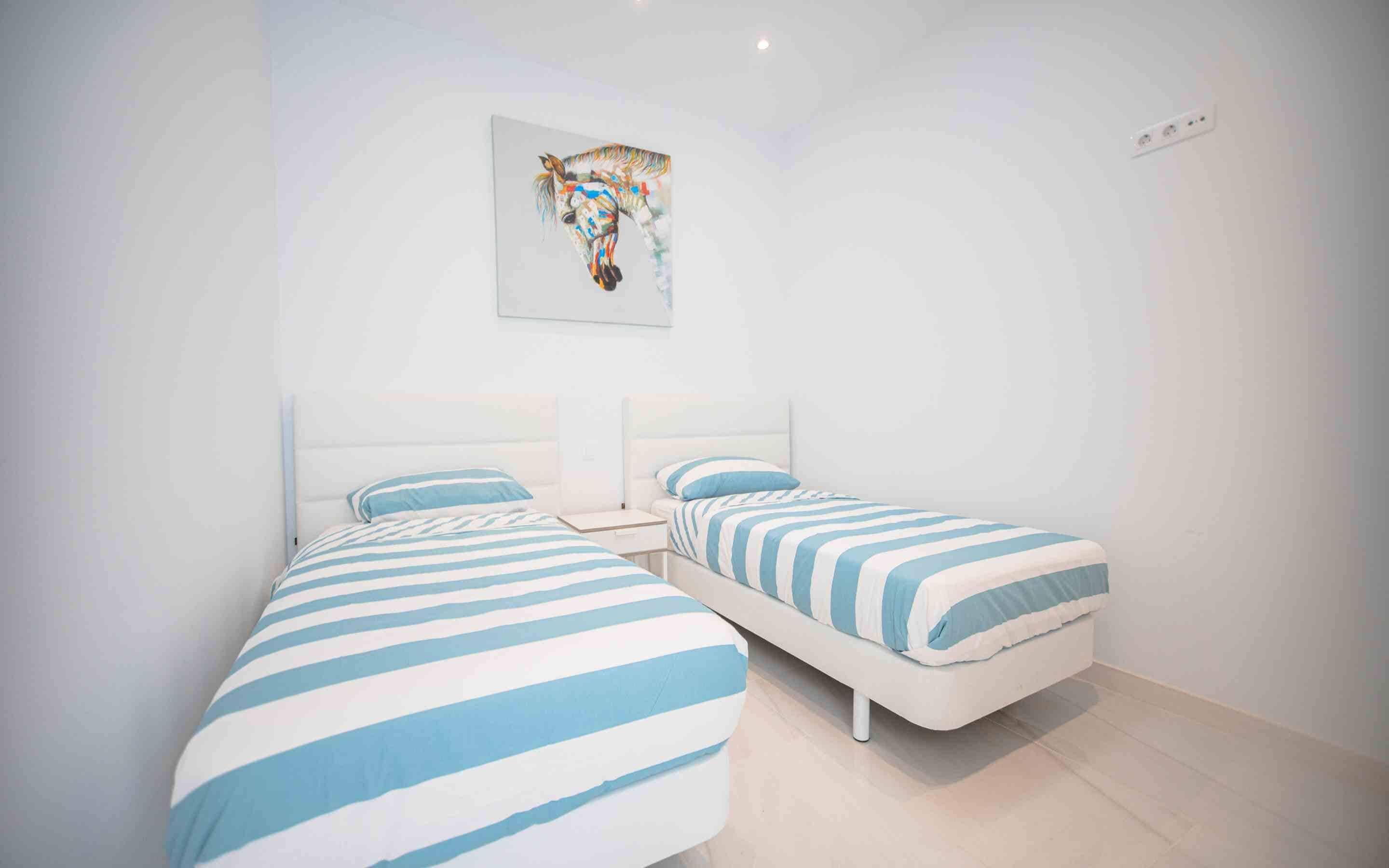 Ein modernes Schlafzimmer mit zwei Betten, jeweils mit blau-weiß gestreifter Bettwäsche, einem weißen Kopfteil und einem Nachttisch.