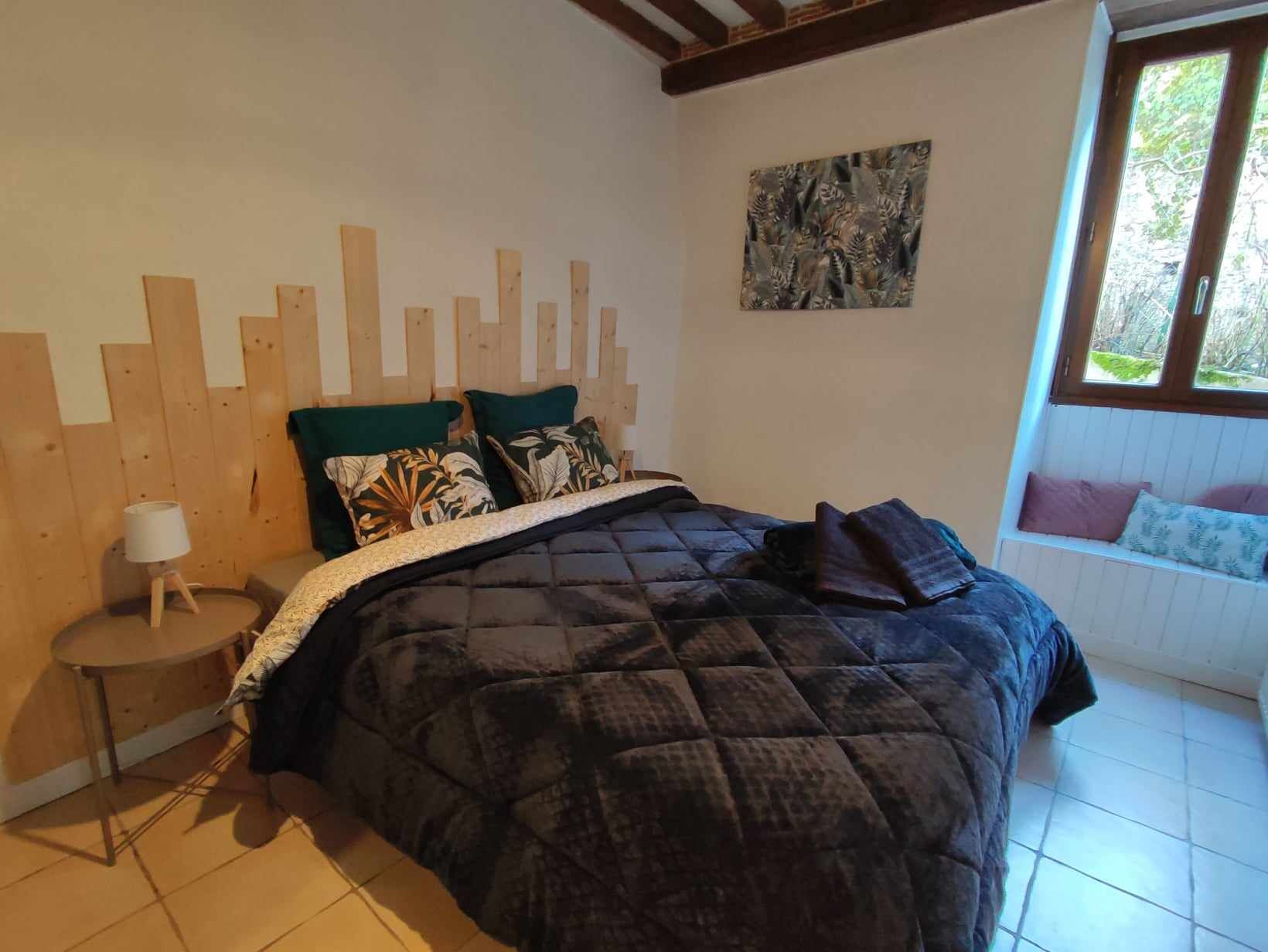 A bedroom with a bed, a nightstand, a window seat, and a wall with a wooden panel design.