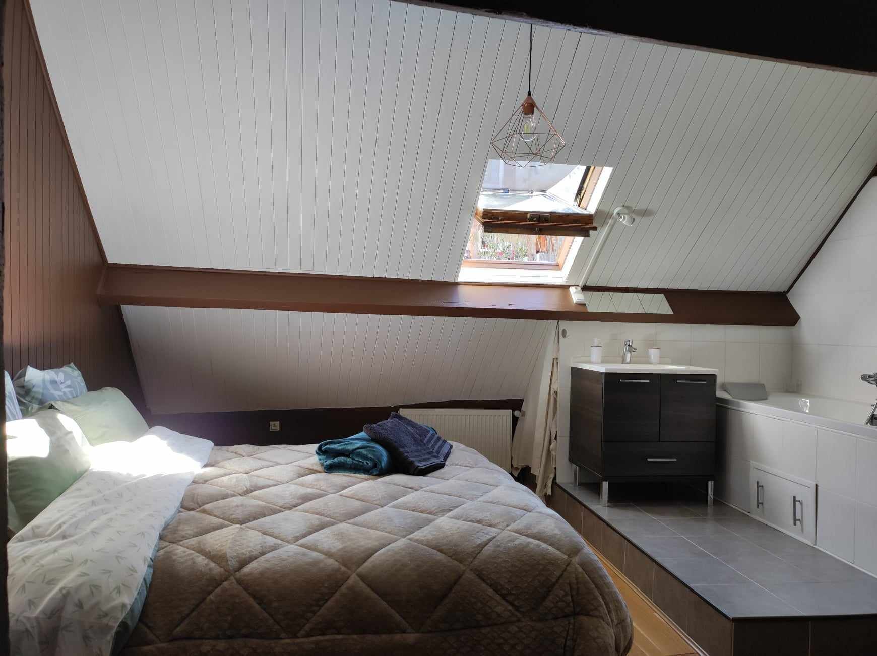 Un dormitori amb sostre inclinat, un llit, televisió i una cuineta petita.