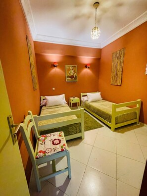Une chambre avec deux lits, une chaise, une petite table et une lampe fixée au mur.