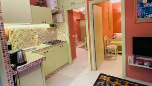 A compact kitchen with a gas stove, a kettle, and a small refrigerator. There is a dining area with a table and chairs, and a TV mounted on the wall. The room has a tiled floor and a colorful rug. - Beautiful Studio in the heart of Casablanca (Casablanca)