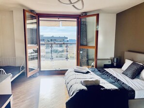 Une chambre d’hôtel moderne avec un grand lit, un petit bureau et un balcon offrant une vue sur la ville.