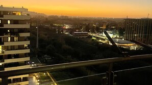 A high-rise building with multiple balconies and a view of a sunset over a cityscape.