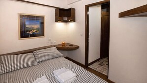 A neatly made bed with checkered bedding and two folded towels, a framed picture on the wall, and a wooden shelf with a candle. - Arachova Nest in the Village by GHH
 (Arachova)