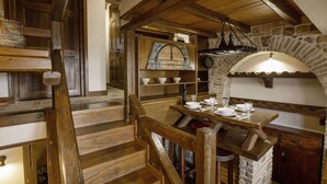 A rustic kitchen with wooden stairs, a stone oven, and a wooden table set for dining. - Arachova Nest in the Village by GHH
 (Arachova)