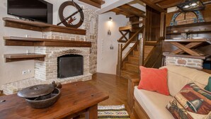 A cozy living room with a fireplace, wooden beams, a television, and a staircase. - Arachova Nest in the Village by GHH
 (Arachova)