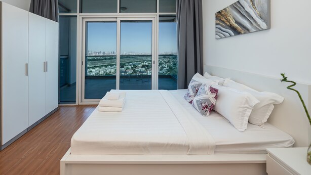 Un dormitorio moderno con una cama grande, vistas de la ciudad a través de ventanales y un candelabro contemporáneo.