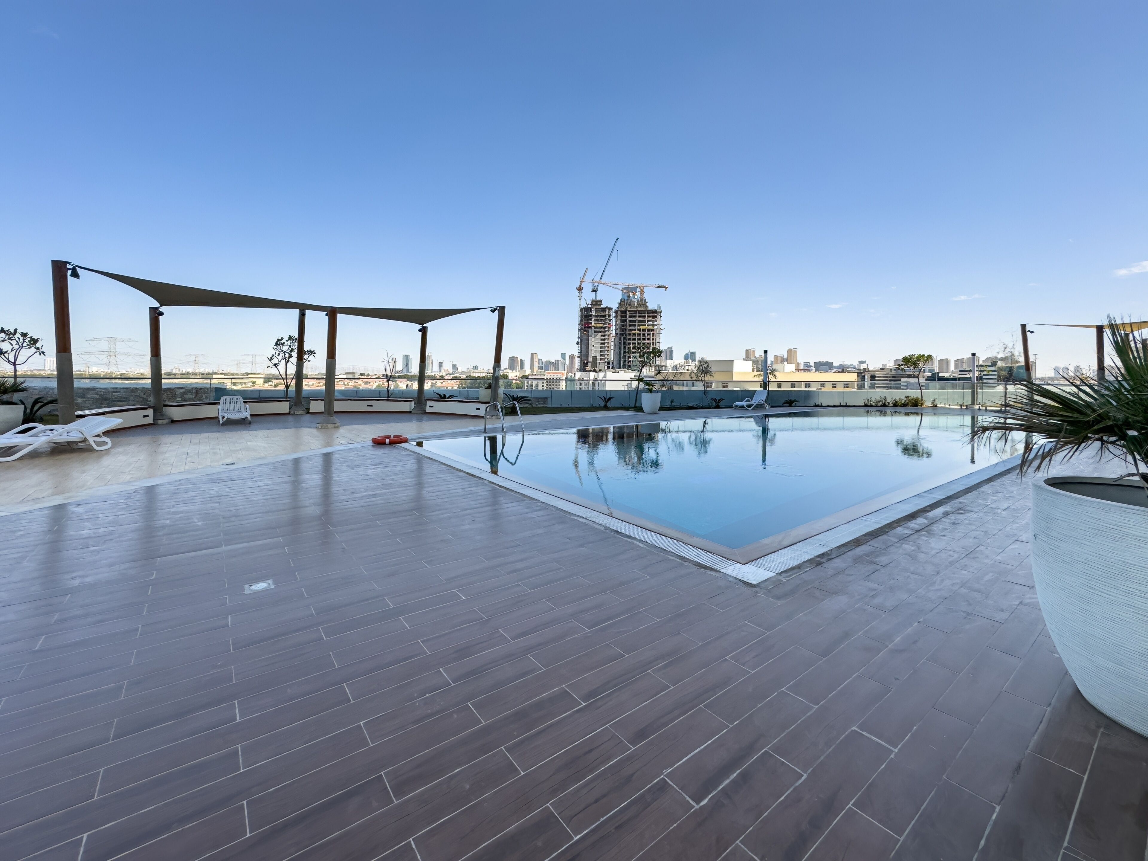 A rooftop swimming pool with lounge chairs and a view of a city skyline and construction site.