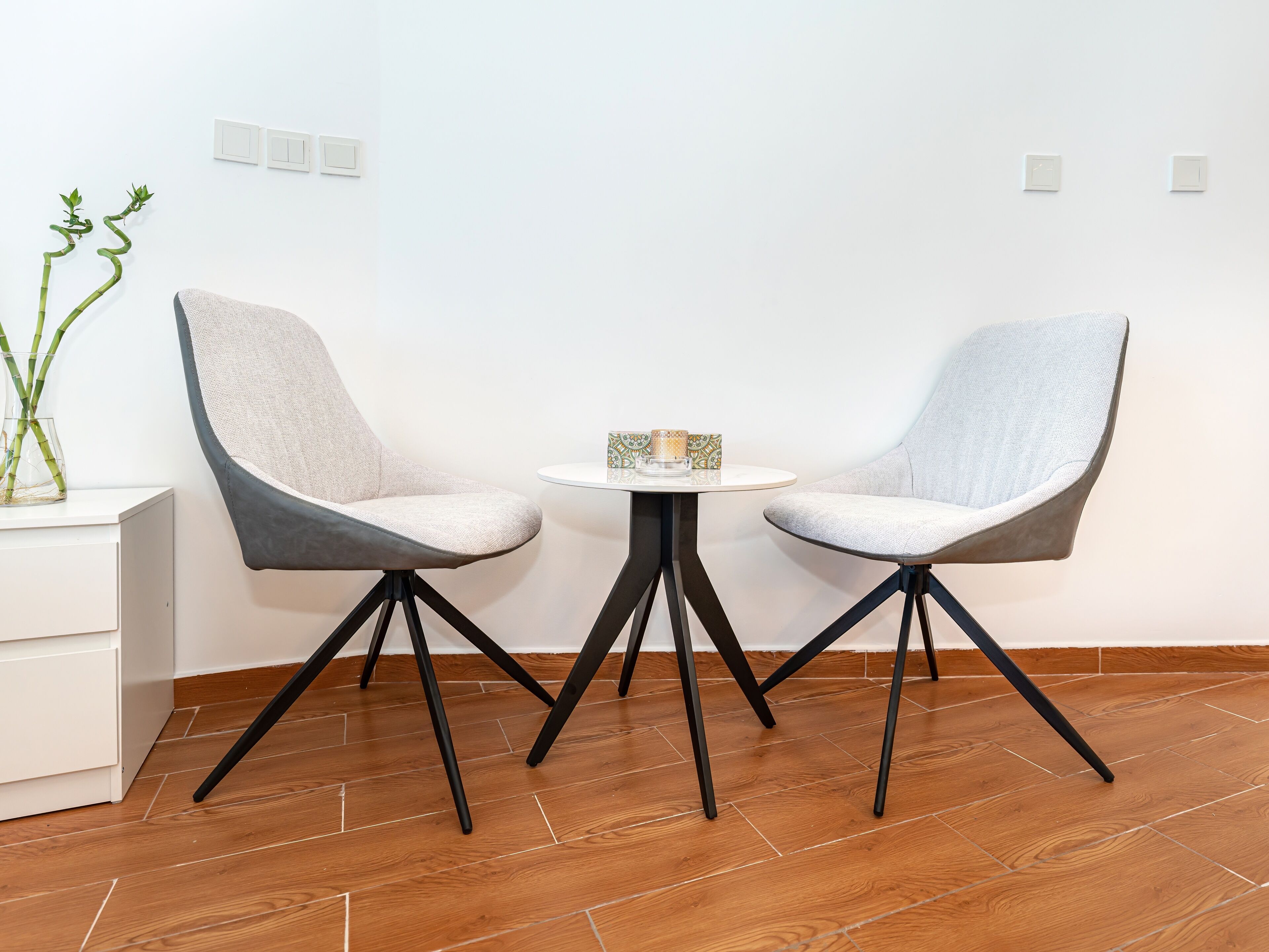 Ein modernes Zimmer mit zwei grau gepolsterten Sesseln, einem kleinen runden Tisch und einem weißen Schrank.