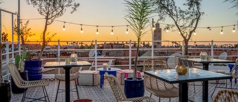 Un patio al aire libre con mesas y sillas, luces colgantes y plantas en macetas.