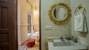 Un baño con un lavamanos blanco, un espejo redondo con un marco similar a una pajita, y un aro para toallas.