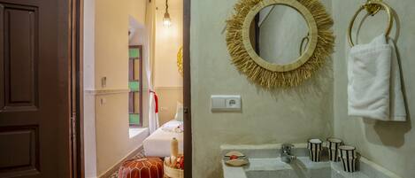 A bathroom with a white sink, a round mirror with a straw-like frame, and a towel ring.
