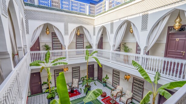 Un patio de varios niveles con arcos blancos, plantas en macetas y suelo de baldosas.