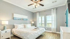 A bedroom with a bed, nightstands, a ceiling fan, a window with curtains, and a view of a balcony. - Porch Paradise - 3 Beach & Water Views, Screened Porch! (Freeport)