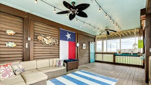 A covered outdoor seating area with a Texas flag, wicker furniture, and a striped rug. - Porch Paradise - 3 Beach & Water Views, Screened Porch! (Freeport)