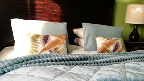 Una cama con colcha azul y almohadas, cabecera oscura y pared verde.