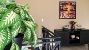 Una habitación con una escalera, una planta en maceta, un cuadro y un armario negro.