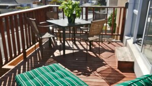 Una terraza de madera con un banco de rayas verdes, una mesa con sillas y una planta en maceta.