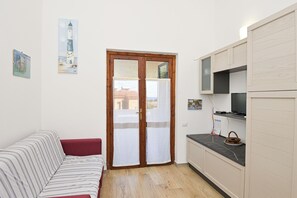 A compact living space with a sofa, a kitchen area with cabinets, a door with a view, and a painting on the wall. - AmareSardegna2 (Muravera - Costa Rei)