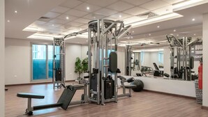 A spacious gym with various exercise equipment, a large mirror, and a wooden floor. - Charming Studio Escape With City View (Dubai)