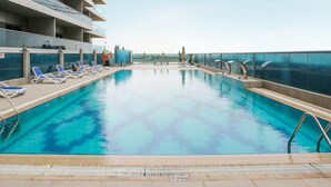 A rooftop swimming pool with clear blue water, surrounded by lounge chairs and a glass balustrade. - Charming Studio Escape With City View (Dubai)