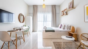 A modern hotel room with a bed, a desk, a chair, a TV, and a window with curtains. - Charming Studio Escape With City View (Dubai)