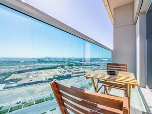 A balcony with a table and chairs, offering a view of a cityscape and a large industrial area.