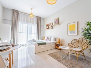 A modern living room with a sofa, a dining table, a wicker chair, and a large window with curtains.