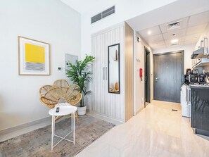 A modern hotel room with a kitchen area, a dining area with a chair and table, and a large mirror.