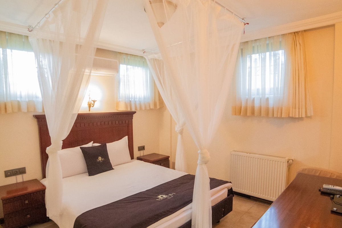 A bedroom with a four-poster bed, a wooden nightstand, a bedside table, and a desk.