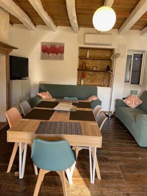 Uma sala de jantar com uma mesa e cadeiras de madeira, um sofá verde e uma televisão sobre um móvel.