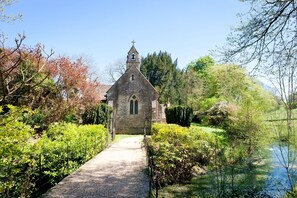 Une église en pierre dotée d’un clocher, entourée d’une végétation luxuriante et accessible par un sentier.
